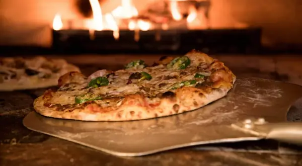Pizza na łopacie przed palącym się piecem.